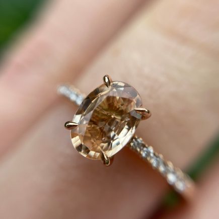 18ct rose gold and oval peach sapphire engagement ring with diamond-set shoulders