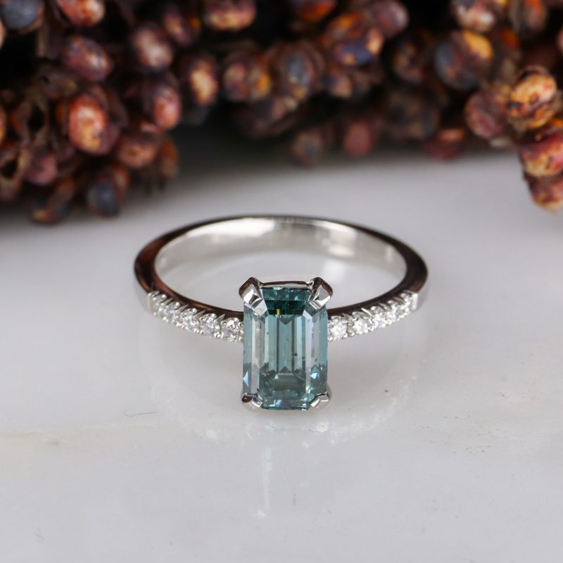 Platinum emerald cut blue diamond rise ring with white diamond shoulders