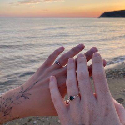 stories in stone part 1 close up of two hands wearing engagement rings at the beach