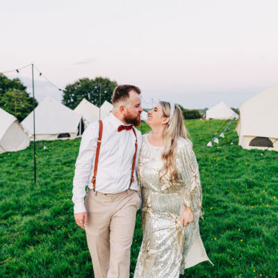 Lucy & Zak couple looking at each other in field with bell tents